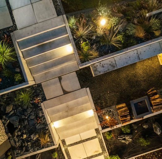 Aerial Night View of a Modern Backyard Garden with Architectural Concrete Elements and a Fireplace. Garden Illuminated by LED Lights Installed in Few Places.